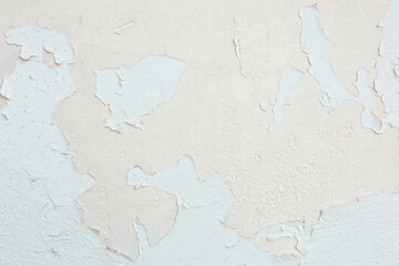 Peeling paint reveals layers of texture on a weathered wall in soft tones