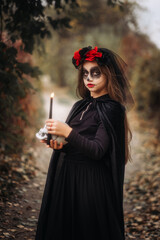 A witch girl with skull makeup holds a candle in a dark forest on Halloween