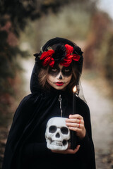A witch girl with skull makeup holds a candle in a dark forest on Halloween
