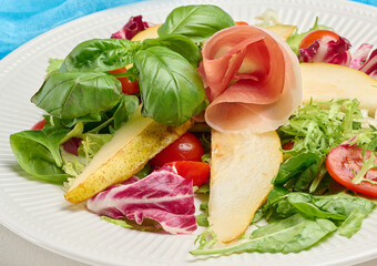 Close up of a gourmet salad with prosciutto, pear slices, cherry tomatoes and fresh mixed greens, close up