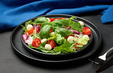 Fresh salad with mixed greens, radicchio and cherry tomatoes, served on a matte black plate.