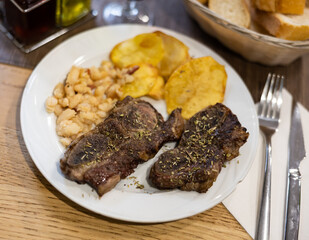 Grilled beef with spices and herbs with potatoes and beans on a white plate. Meat dish according to a traditional Spanish recipe