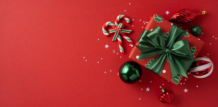 A festive Christmas gift banner with a green bow sits among decorative ornaments and candy canes on a red backdrop, capturing holiday cheer, festive mood, and seasonal celebration