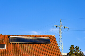 Solarthermieanlage auf rotem Hausdach vor blauem Hommel mit Strommast im Hintergrund