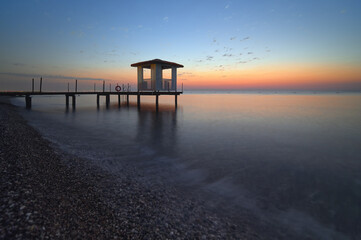 Serene sunrise pier silhouette with beach cabana over tranquil sea landscape view nature. Goynuk, Turkey. High quality photo