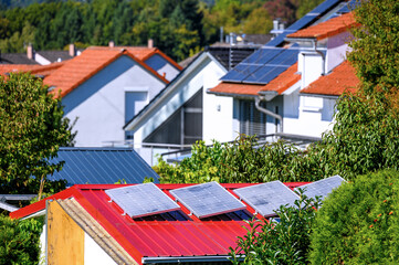 Balkonkraftwerk auf Gartenhaus mit rotem Dach sowie Wohnh&auml;user mit Solard&auml;chern zur umweltfreundlichen Stromerzeugung	