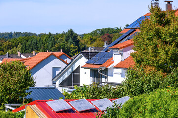 Balkonkraftwerk auf Gartenhaus mit rotem Dach sowie Wohnh&auml;user mit Solard&auml;chern zur umweltfreundlichen Stromerzeugung	