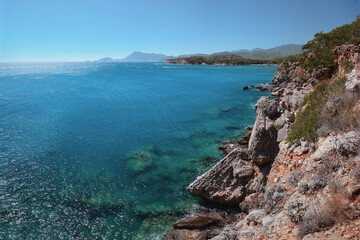 The image captures a breathtaking view of rocky cliffs overlooking a serene blue sea, the coastline under a clear sky. West coast of the Gulf of Antalya in southern Turkey. High quality photo