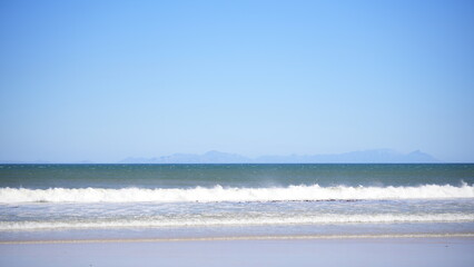 Ocean waves on sandy beach with clear blue sky, summer seascape and travel background
