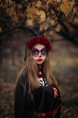 Witch with skull makeup in a dark forest on Halloween.