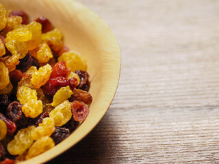 A bowl of dried fruit with yellow and red raisins, cranberries. The bowl is on a wooden table. Natural high sugar and glucose content. Popular snack.
