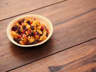 A bowl of dried fruit with yellow and red raisins, cranberries. The bowl is on a wooden table. Natural high sugar and glucose content. Popular snack.