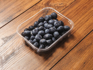 A plastic tray of blueberries sits on a wooden table. The tray is clear and filled with fresh organic fruits ready for consumption. Healthy diet concept. Natural product.