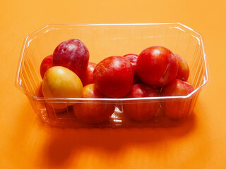 Fresh pure nectarine with glossy skin in a plastic basket on warm orange background. Agriculture product ready to eat and for sale. Food chain supply. Clean ripe organic product carefully selected.