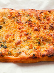 A piece of bread with cheese on it is sitting on a piece of paper. Cooked pizza is brown and the cheese is white. Popular Italian style dish.