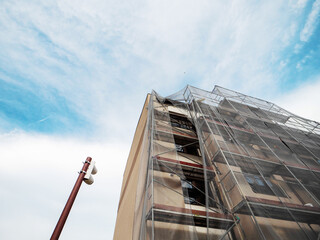 Residential apartment building during facade repair or renovation with scaffolding around it in safety mesh. Property upgrade, job increasing value of the home. Construction site.