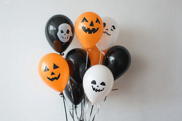 Halloween balloons: orange pumpkins, white ghosts, and black skulls against a white wall.