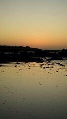 Scenic sunset over rocky coastline with calm ocean water reflecting golden sky, tranquil seascape
