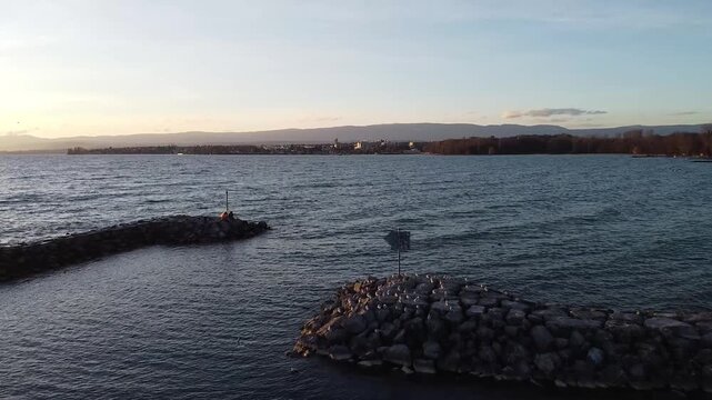 Aerial view of sturdy piers and wave breakers at Lausanne, protecting the calm waters of Lake Geneva. The stone structures gleam under the sunlight against the gentle waves.