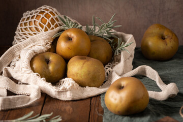 A rustic still life with russet apples in a string bag, evoking a cozy and autumnal mood on a dark...