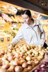 Selective middle-aged female buyer purchasing potatoes in grocery store with large assortment