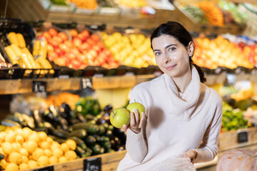 Young woman buyer choosing fresh apples in vegetable shop