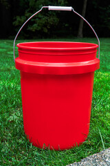 Five gallon, multipurpose red bucket. This type of bucket is offered at many big box stores and other retail outlets. Isolated against a grass background. The bucket photo has copy space room. 