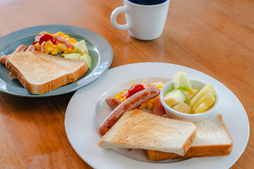Western breakfast with toast, scrambled eggs, sausages, fruit and coffee
