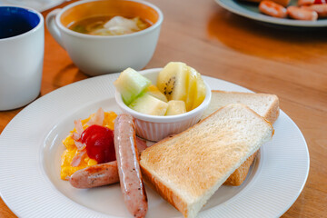 Western breakfast with toast, scrambled eggs, sausages, fruit and coffee
