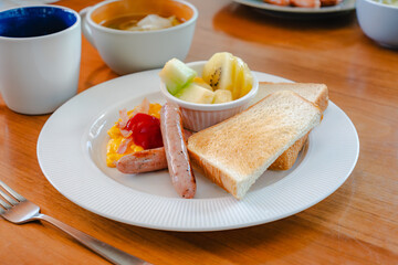 Western breakfast with toast, scrambled eggs, sausages, fruit and coffee
