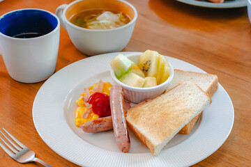 Western breakfast with toast, scrambled eggs, sausages, fruit and coffee
