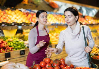 Woman consults with a seller about the choice of tomatoes in a supermarket. Buyer asks the seller which tomatoes to choose