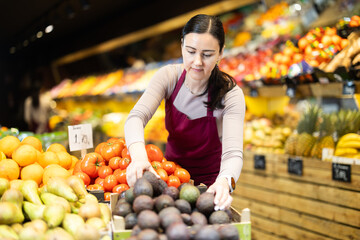 Female salesperson carefully places ripe passion fruit on the counter of a grocery supermarket
