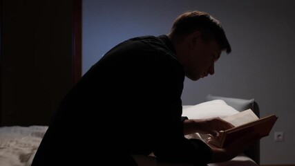 Young man reading a book in a dark room
