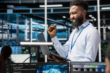 Happy data center admin celebrating after managing to setup machine learning systems handling information. Cheerful IT expert pleased after training neural networks to improve server farm operations