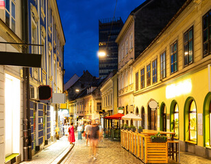 Obraz premium Bend of Tkalciceva street street, evening atmosphere in pedestrian zone of central district of Zagreb. Signs of cafes and restaurants shine brightly and attractively, people are walking.