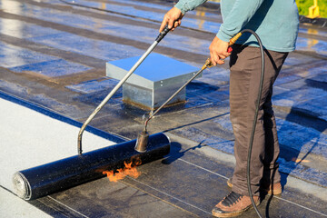 Roofer applying torch to bitumen membrane on torch down roof