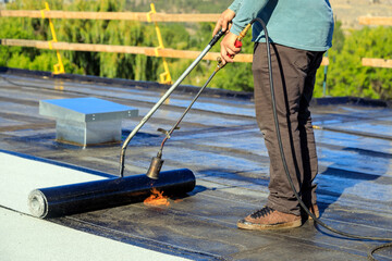 Roofer applying torch to bitumen membrane on torch down roof