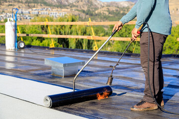 Roofer applying torch to bitumen membrane on torch down roof