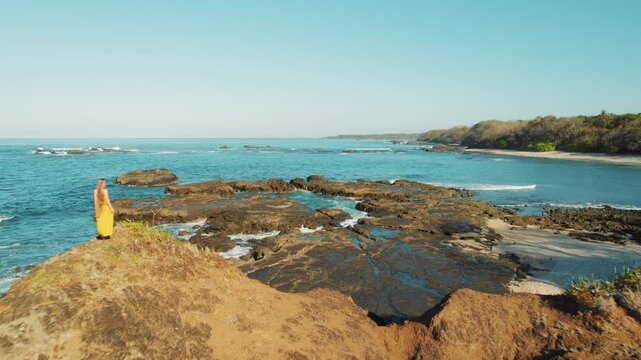Woman walking on coastal rocks with ocean waves and blue sky in Costa Rica