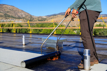 Roofer applying torch to bitumen membrane on torch down roof