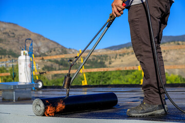 Roofer applying torch to bitumen membrane on torch down roof