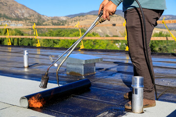 Roofer applying torch to bitumen membrane on torch down roof
