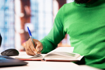 Close up of man writing personal notes in apartment workspace. Productive person sitting at home...