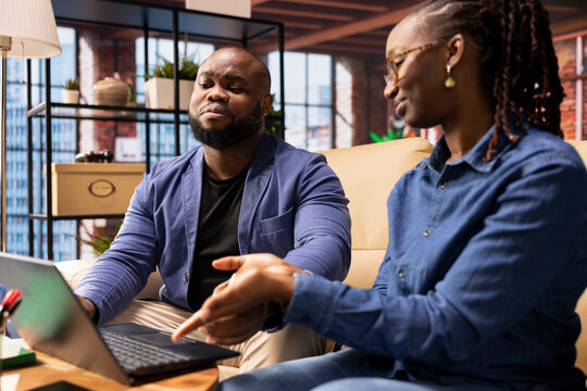 African american people sitting on sofa to collaborate on a business idea, using modern technology and tools to analyze trends and boost success. Freelancers improving workflow efficiently. - Powered by Adobe