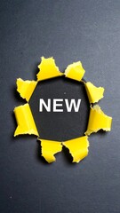 Yellow paper cutout with the word "NEW" on dark gray background