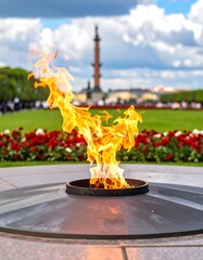 Eternal flame in a park setting.  Flaming memorial with a cloudy sky in the background.  Circular metal base.  Flowerbeds surround the base.  Focus on the flame