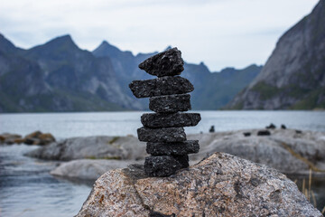 Balanced stone cairn on a rocky coastline with mountains and sea in the background in Norway.