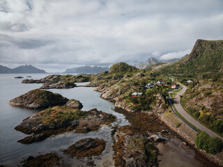 Fototapeta premium Drone photo of small Norway fishing village on rocky coast surrounded by mountains and fjord waters.