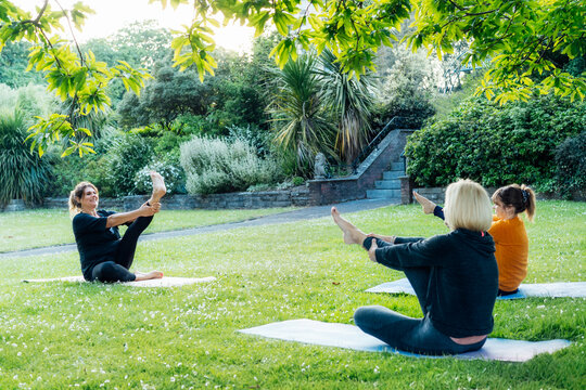 Female yoga class in park. Group of diverse women doing stretching pose exercising together with instructor on green grass lawn. Sport activity for health, wellbeing, mental health. Selective focus